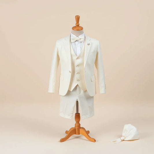 Costum de botez pentru băiat, cu sacou alb, vestă asortată și accesorii elegante, aranjat pe suport minimalist.